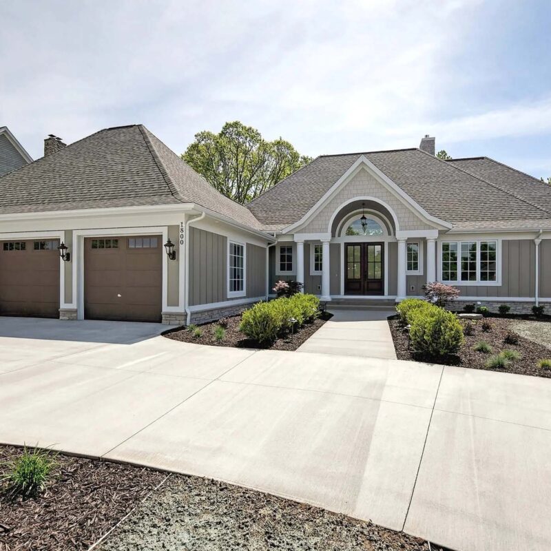 Wide angle image of a new grey house that features a three car garage